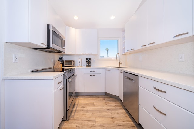 kitchen with light wood-type flooring, appliances with stainless steel finishes, white cabinets, sink, and tasteful backsplash