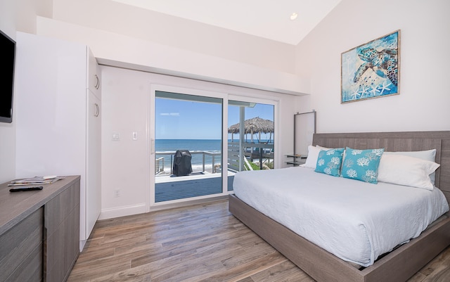 bedroom featuring access to outside, lofted ceiling, a water view, and hardwood / wood-style floors