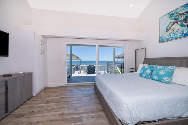 bedroom with a water view, multiple windows, access to outside, and wood-type flooring