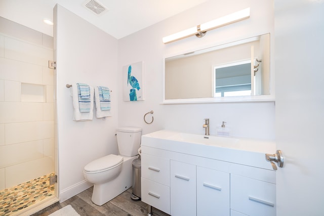 bathroom with wood-type flooring, tiled shower, oversized vanity, and toilet