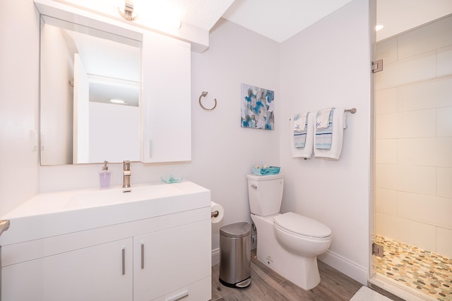 bathroom with tiled shower, wood-type flooring, toilet, and vanity