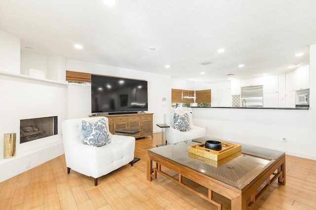 living area featuring light wood finished floors, a fireplace with raised hearth, a textured ceiling, and recessed lighting