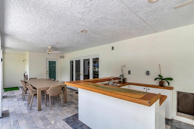 kitchen featuring a textured ceiling, a sink, a ceiling fan, wooden counters, and french doors