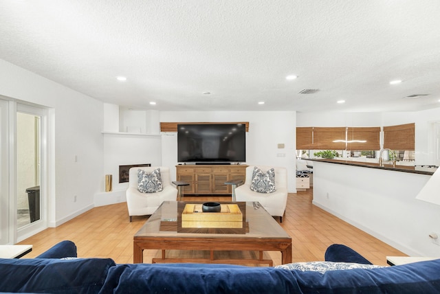 living area featuring light wood-style flooring, visible vents, a fireplace with raised hearth, and a textured ceiling