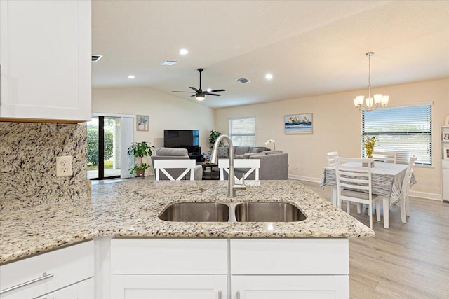 kitchen featuring white cabinets, ceiling fan with notable chandelier, sink, decorative backsplash, and light stone countertops