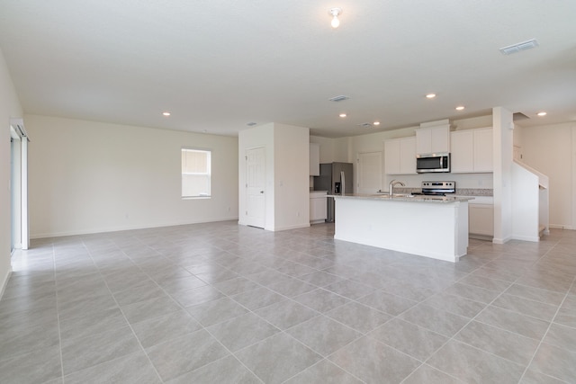 kitchen featuring a kitchen island with sink, light stone countertops, light tile patterned flooring, white cabinetry, and stainless steel appliances