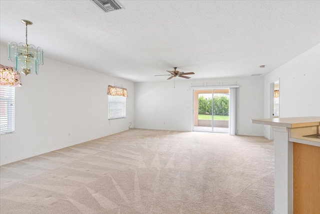 unfurnished living room featuring light colored carpet, plenty of natural light, ceiling fan with notable chandelier, and a textured ceiling