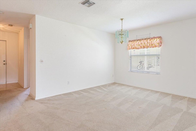 carpeted spare room with a textured ceiling and a notable chandelier