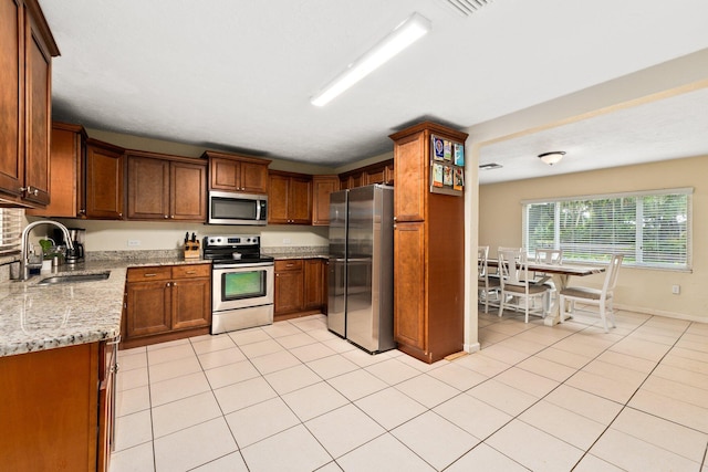 kitchen with appliances with stainless steel finishes, light tile patterned floors, light stone counters, and sink