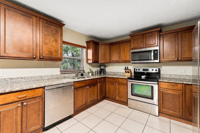 kitchen featuring light stone counters, sink, light tile patterned floors, and appliances with stainless steel finishes