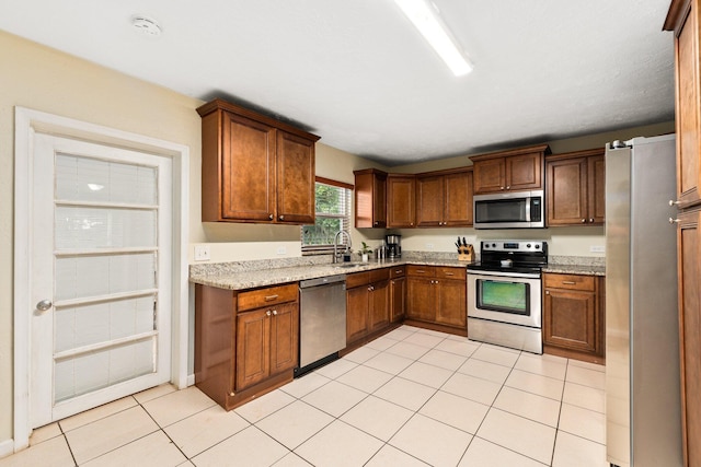 kitchen with light stone countertops, sink, light tile patterned flooring, and appliances with stainless steel finishes