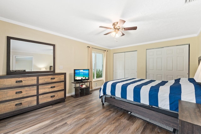 bedroom with ceiling fan, dark hardwood / wood-style floors, ornamental molding, and two closets