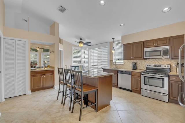 kitchen featuring light stone countertops, a center island, stainless steel appliances, pendant lighting, and a breakfast bar area