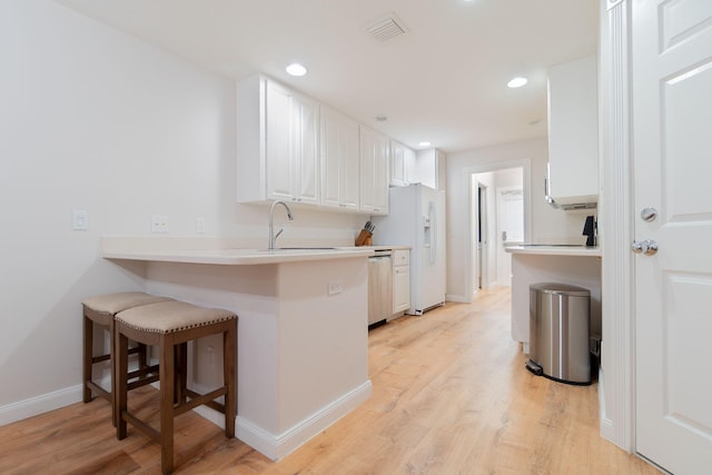 kitchen featuring white cabinetry, light hardwood / wood-style floors, a kitchen bar, and kitchen peninsula