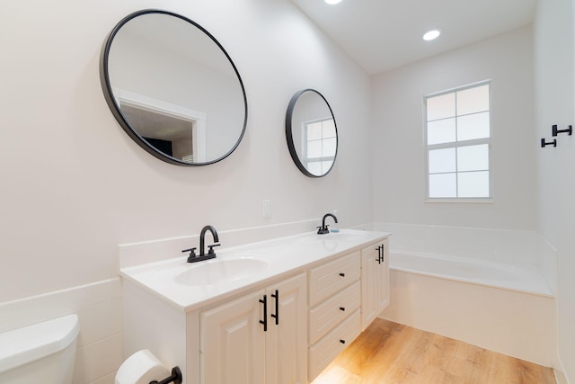 bathroom with double vanity, a washtub, wood-type flooring, and toilet