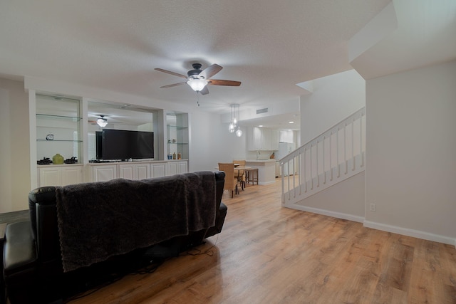 living room with light hardwood / wood-style floors, built in shelves, ceiling fan, and a textured ceiling