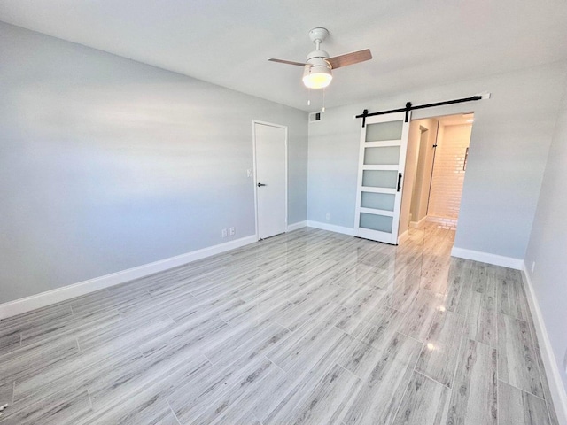 unfurnished room featuring ceiling fan, a barn door, and light hardwood / wood-style floors