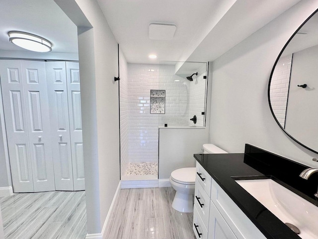 bathroom featuring vanity, tiled shower, hardwood / wood-style floors, and toilet