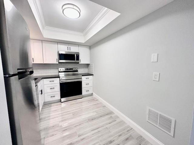 kitchen with white cabinetry, decorative backsplash, ornamental molding, a tray ceiling, and stainless steel appliances