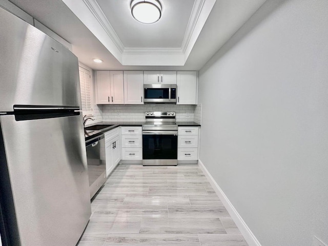 kitchen with crown molding, backsplash, stainless steel appliances, a tray ceiling, and white cabinets