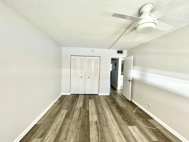 unfurnished bedroom featuring ceiling fan, a closet, dark wood-type flooring, and a textured ceiling