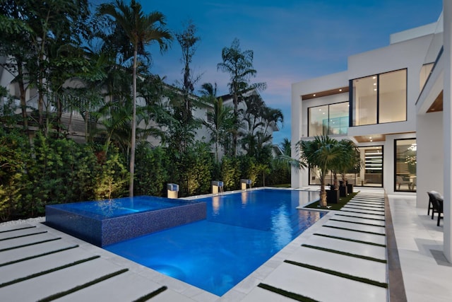 pool at dusk featuring a patio area and an in ground hot tub