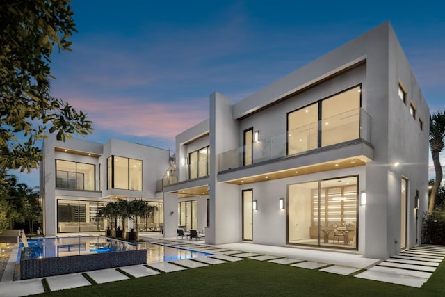 back house at dusk with a yard, a balcony, a patio area, and a pool with hot tub