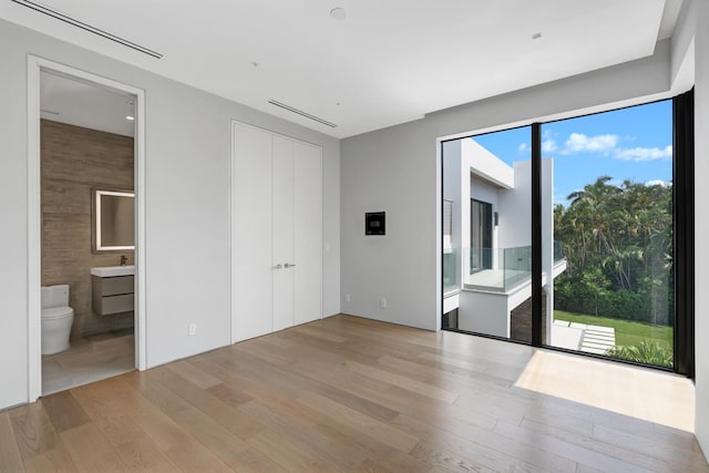 unfurnished bedroom featuring ensuite bath, a closet, and light hardwood / wood-style flooring