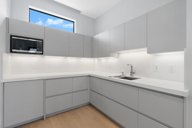 kitchen featuring gray cabinets, stainless steel microwave, light wood-type flooring, and sink