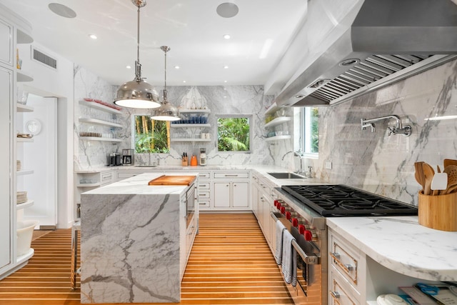 kitchen with designer range, wall chimney exhaust hood, white cabinets, and tasteful backsplash