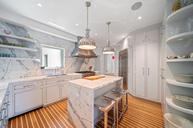 kitchen with wall chimney range hood, light wood-type flooring, a kitchen island, backsplash, and sink