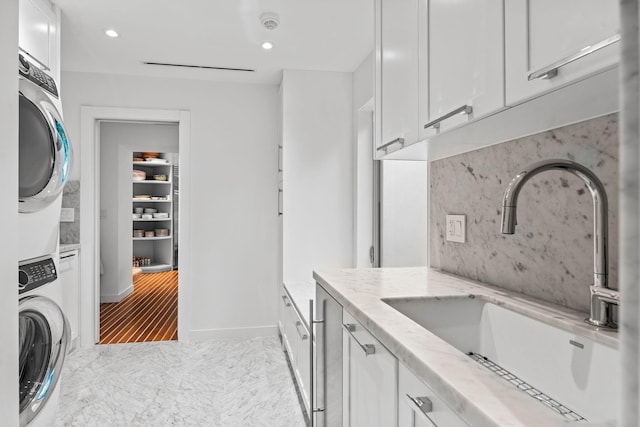 interior space featuring sink, stacked washer and clothes dryer, white cabinetry, and light tile floors