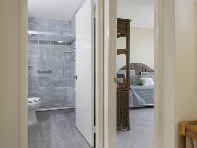 bathroom with hardwood / wood-style flooring, a shower with shower door, a textured ceiling, and toilet