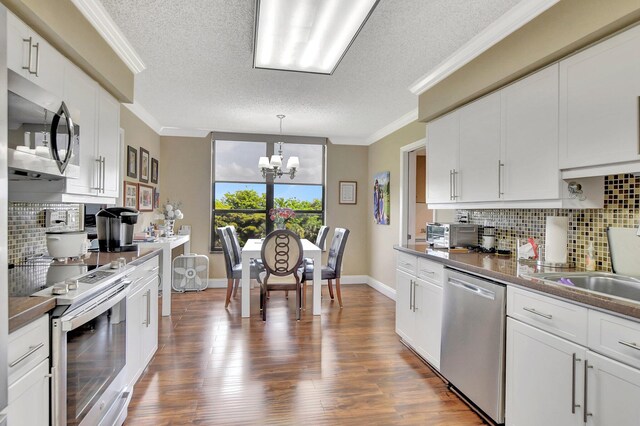 kitchen with appliances with stainless steel finishes, tasteful backsplash, white cabinets, an inviting chandelier, and wood-type flooring