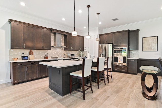 kitchen featuring dark brown cabinetry, decorative light fixtures, ornamental molding, stainless steel appliances, and wall chimney range hood