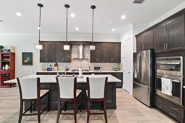 kitchen with wall chimney exhaust hood, decorative light fixtures, dark brown cabinets, a center island with sink, and stainless steel appliances