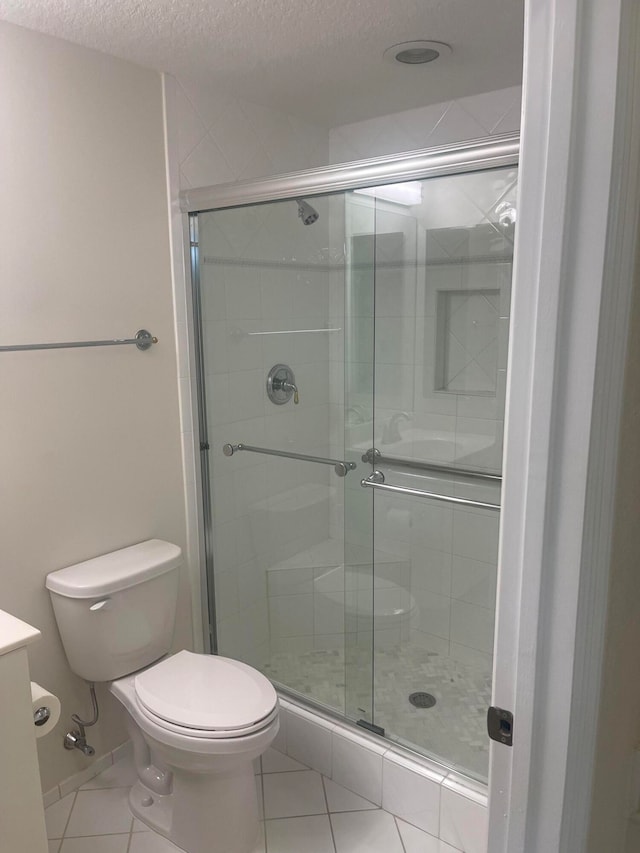 bathroom featuring a shower with door, tile patterned floors, toilet, vanity, and a textured ceiling