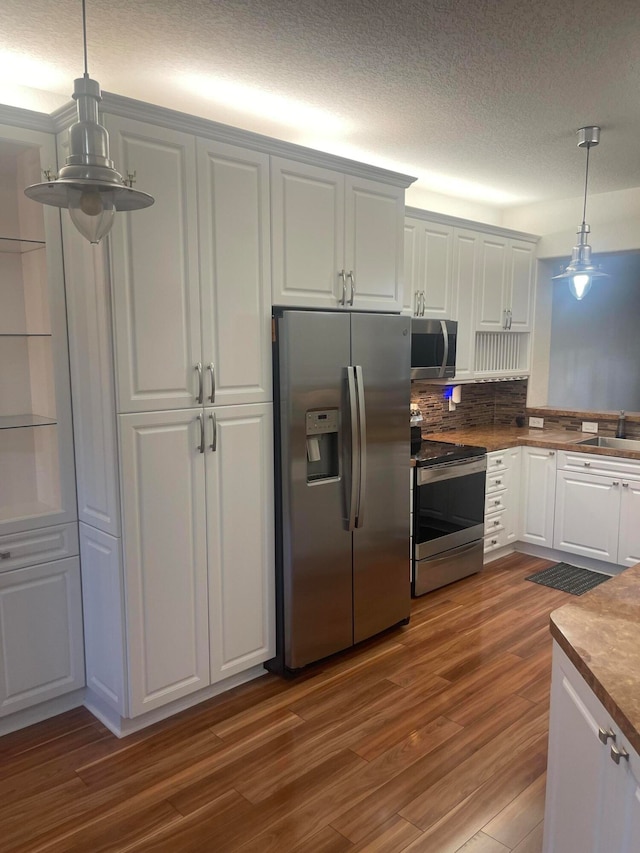 kitchen with dark wood-type flooring, stainless steel appliances, decorative light fixtures, white cabinets, and a textured ceiling