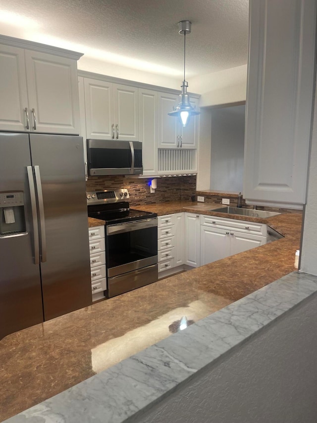 kitchen featuring hanging light fixtures, backsplash, appliances with stainless steel finishes, white cabinetry, and sink