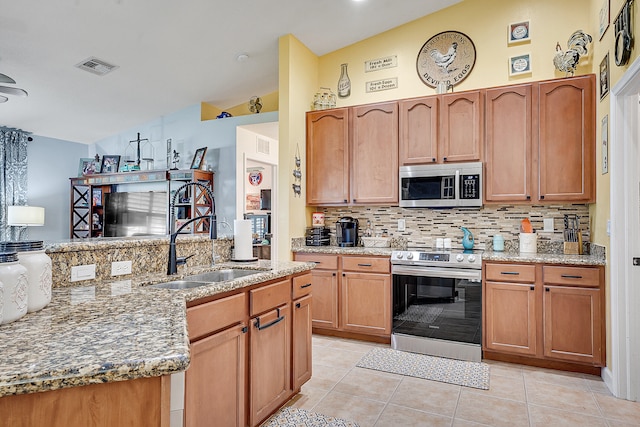 kitchen featuring light tile flooring, tasteful backsplash, light stone countertops, appliances with stainless steel finishes, and sink