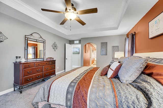 carpeted bedroom with ceiling fan, a raised ceiling, crown molding, and ensuite bath