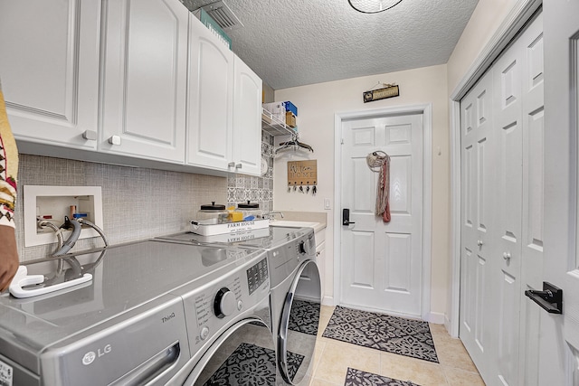 washroom with cabinets, washer and clothes dryer, light tile floors, washer hookup, and a textured ceiling