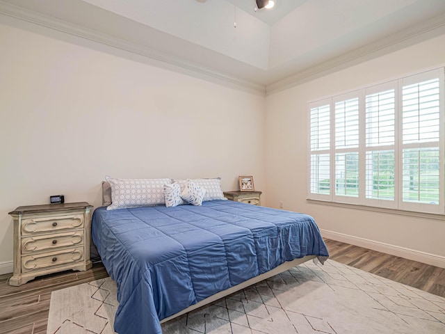 bedroom with a raised ceiling, wood-type flooring, ornamental molding, and ceiling fan