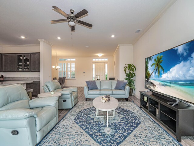 living room with light wood-type flooring, ornamental molding, and ceiling fan with notable chandelier