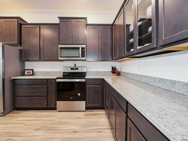 kitchen with light stone counters, crown molding, stainless steel appliances, and dark brown cabinetry