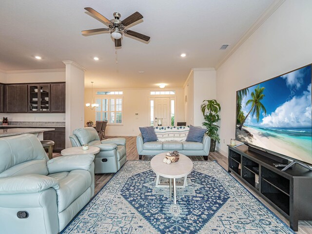 living room featuring light wood-type flooring, ceiling fan with notable chandelier, and crown molding