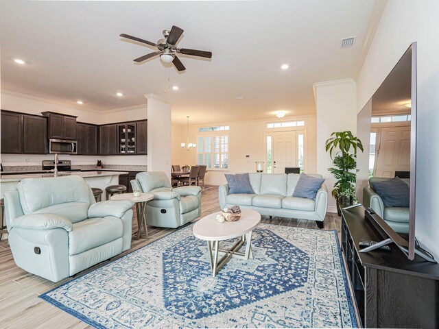 living room with light wood-type flooring, ceiling fan with notable chandelier, and crown molding