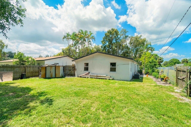 rear view of property with cooling unit, a storage unit, and a yard