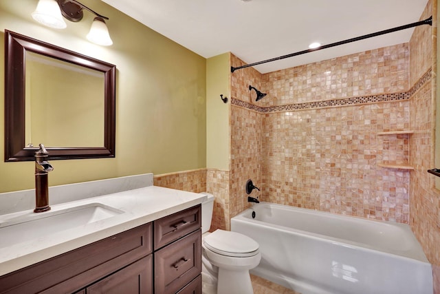 full bathroom featuring tiled shower / bath, vanity, toilet, and tile walls