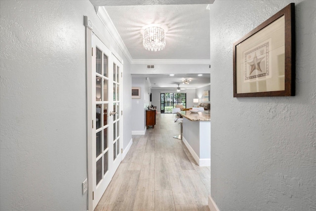 corridor featuring light hardwood / wood-style floors, french doors, ornamental molding, a textured ceiling, and a notable chandelier